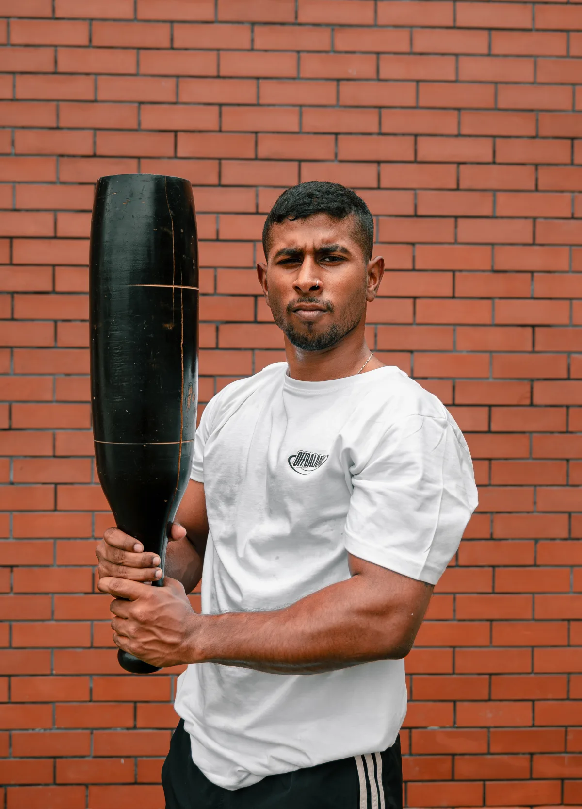 CJ holding a gada in front of an Off Balance brick wall